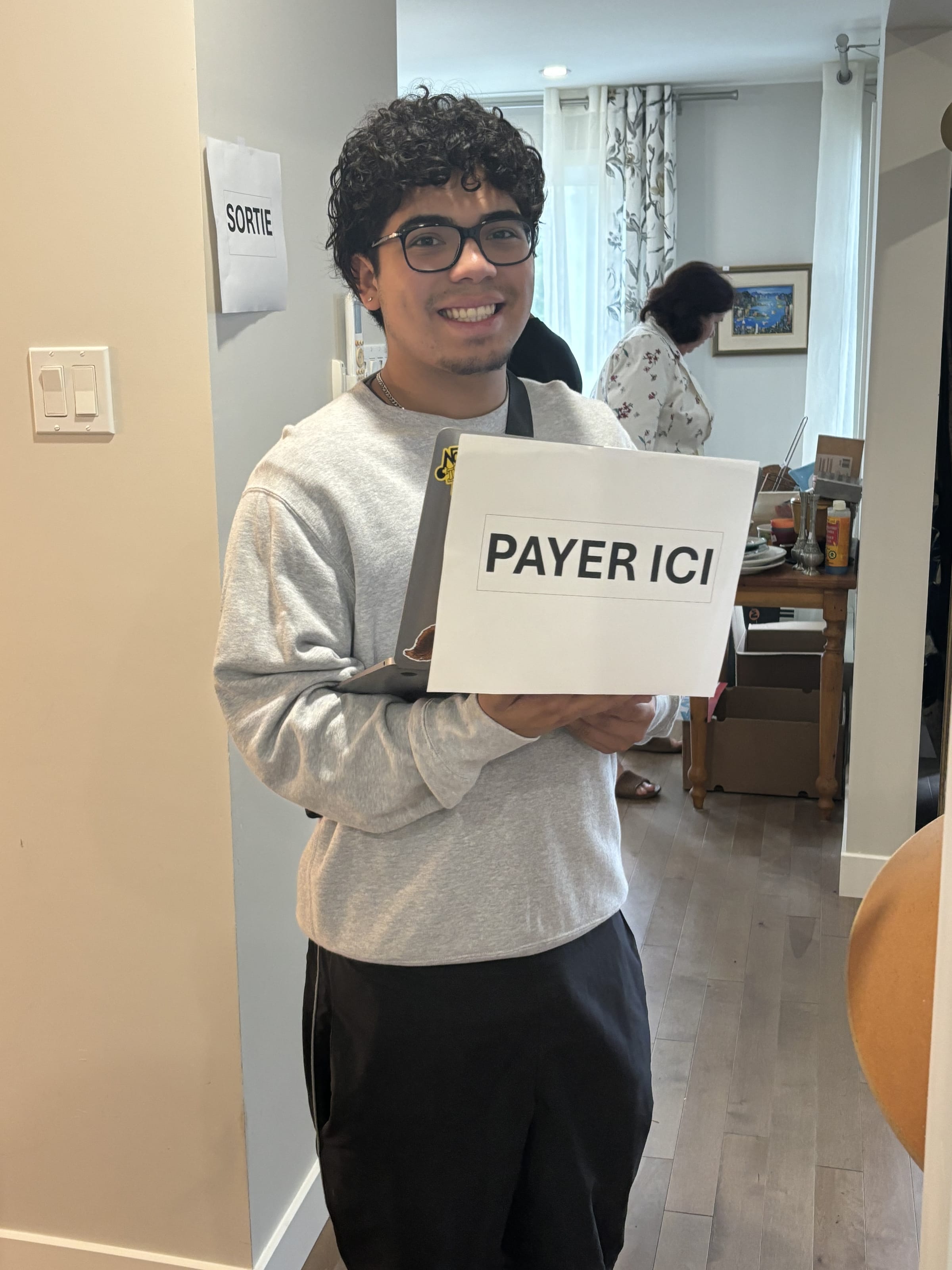 Une personne tient un panneau « Payer ici » dans l'entrée d'une maison, pendant la vente