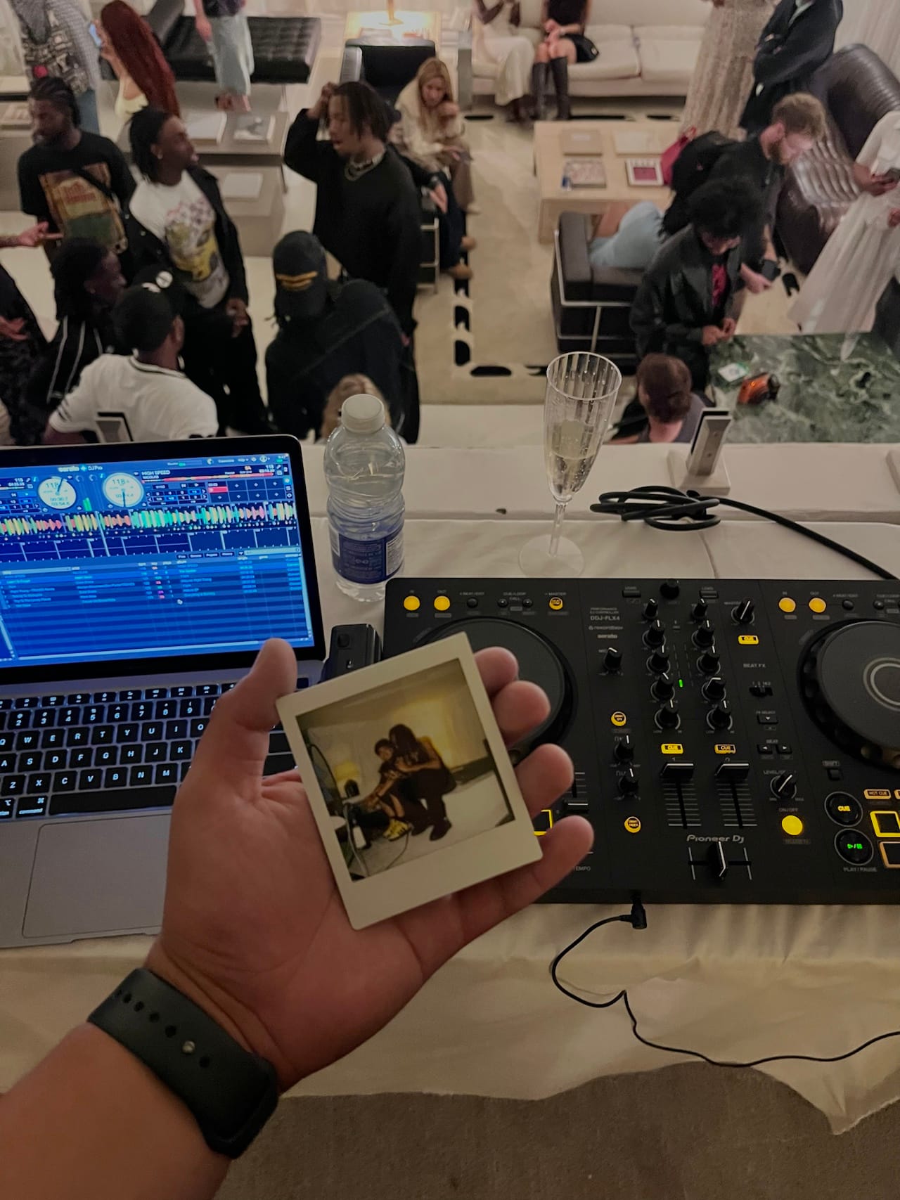 Une main tient une photo instantanée devant une console de DJ, avec la foule derrière