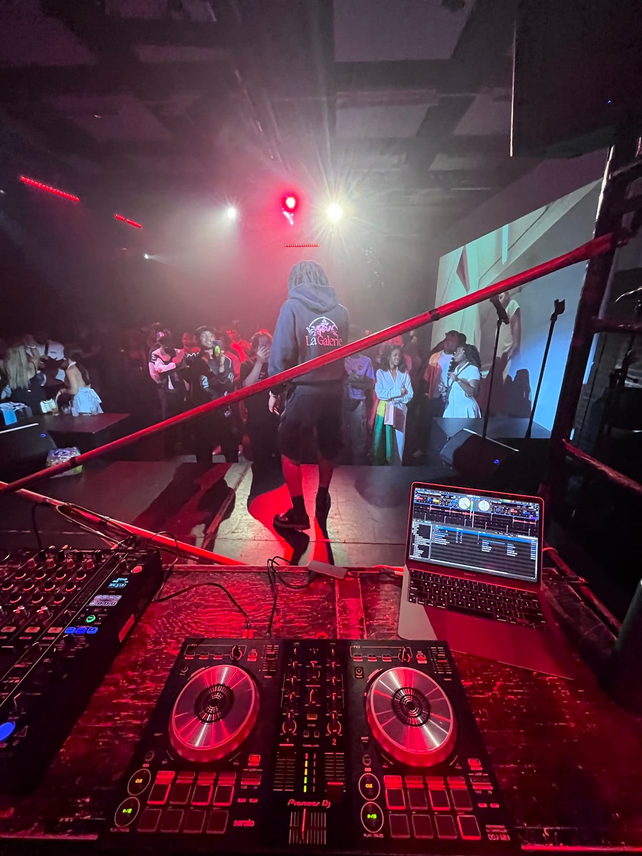 Une console de DJ éclairée en rouge, avec le public au fond pendant une soirée
